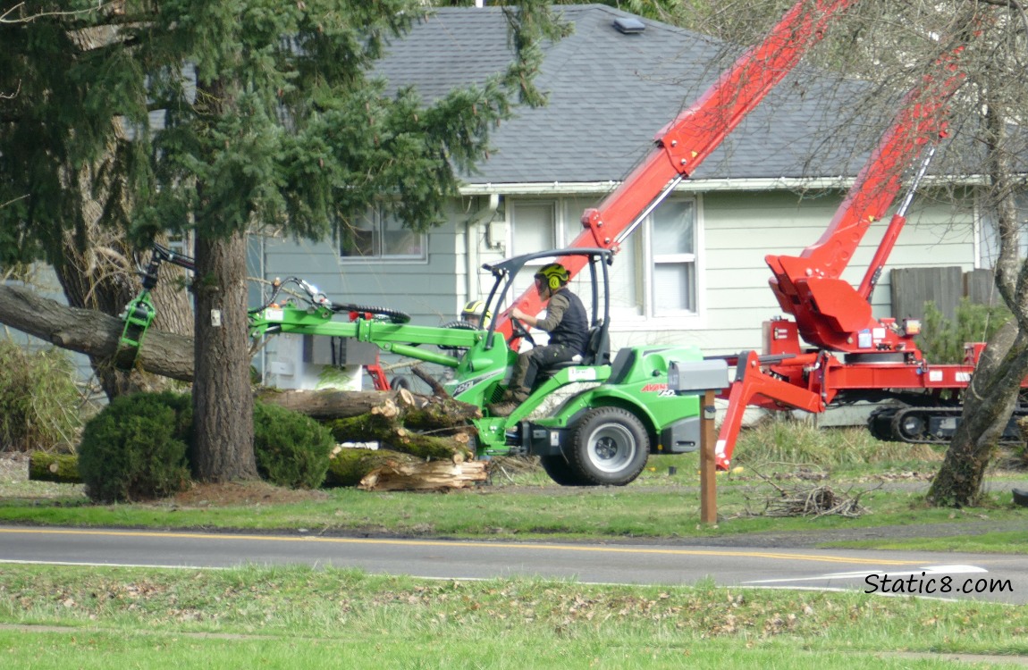 A small claw machine driven by a man, picking up a section of tree trunk