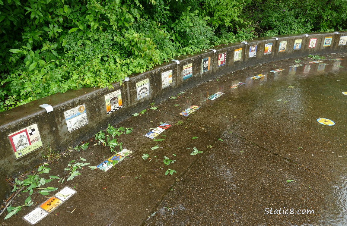 Colourful tiles along a low sitting wall with green bushes behind