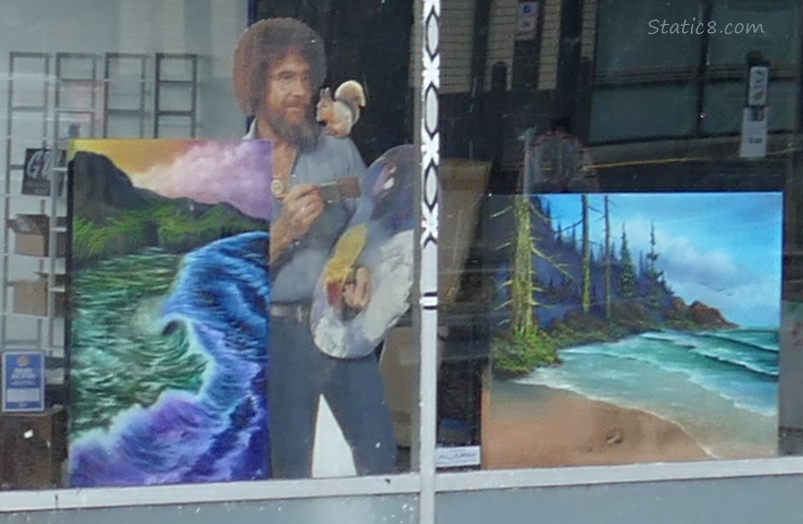 Cardboard Bob Ross in a display window with paintings of Oregon Coast ocean views