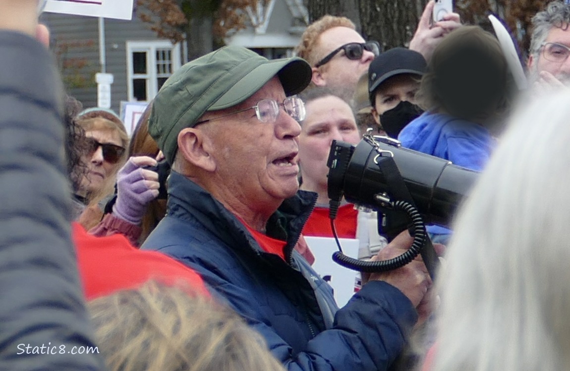Peter Defazio speaking into a loud speaker, surrounded by protesters