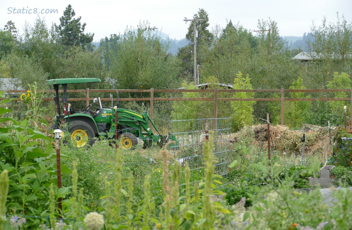 John Deere tractor with a front loader, behind garden plots