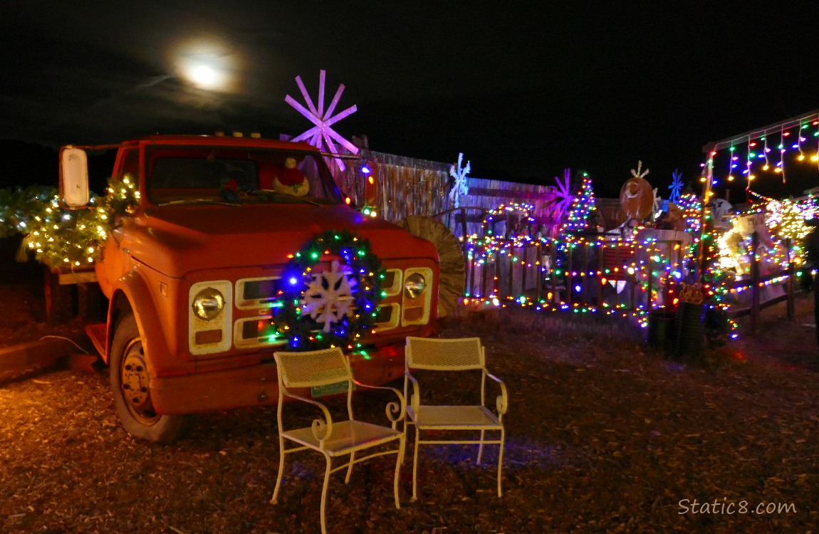 Old truck lit up with christmas lights with the moon in the sky