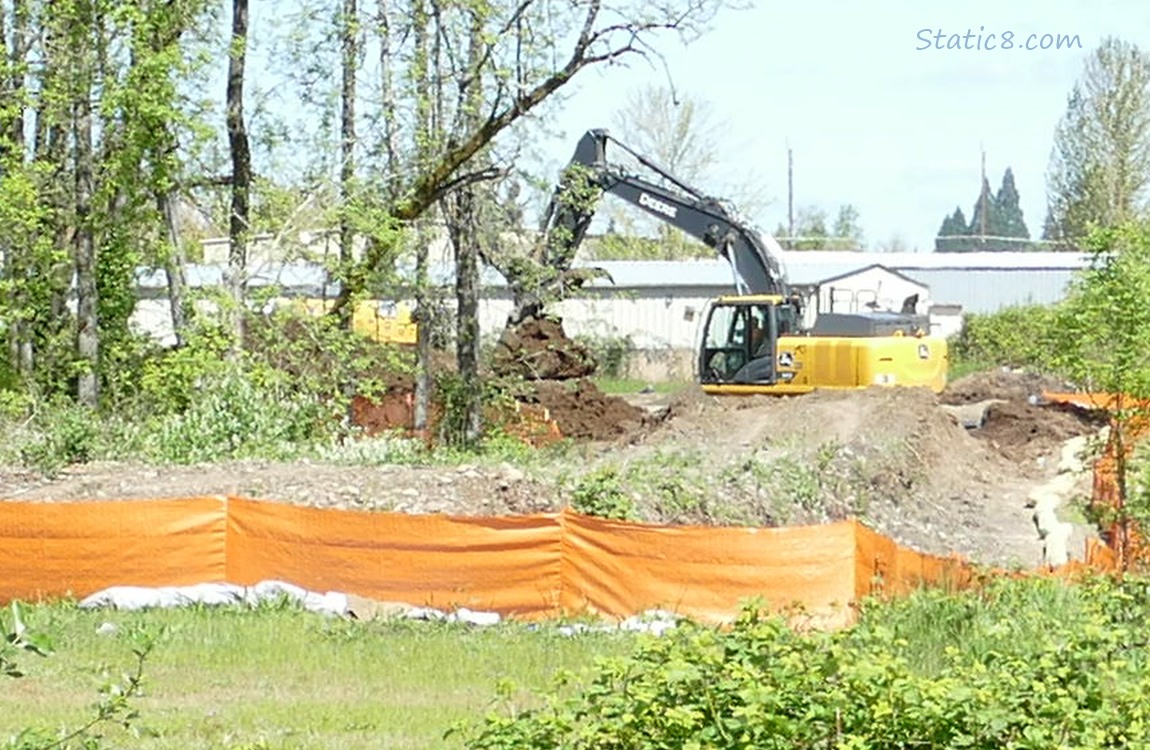 Digging machine and trees past an orange fence