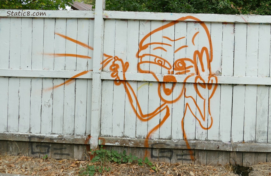 Graffiti alien with a spray can on a white fence