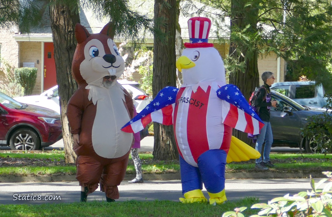 Two people in inflatable costumes dancing under the trees