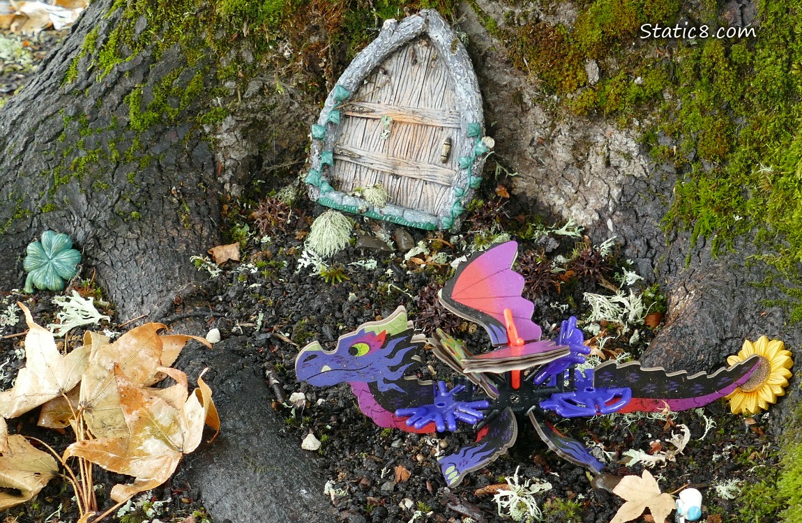 Fairy door into the base of a tree trunk with a cardboard dragon sitting next to it