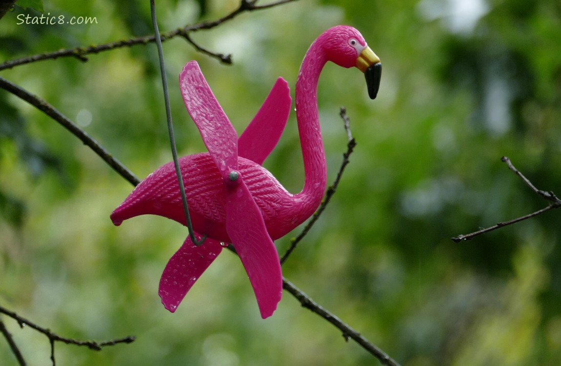 Pink, plastic flamingo with rotating wings hanging from a wire in a tree